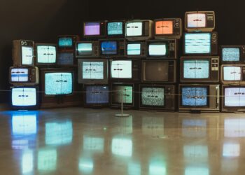 Karanlık bir odada farklı boyutlarda eski ve yeni televizyon ekranları.