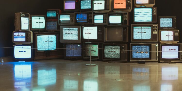 Karanlık bir odada farklı boyutlarda eski ve yeni televizyon ekranları.