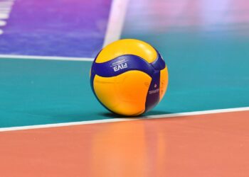 Saha çizgisi üzerinde duran sarı ve mavi renkli bir voleybol topu.