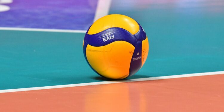 Saha çizgisi üzerinde duran sarı ve mavi renkli bir voleybol topu.