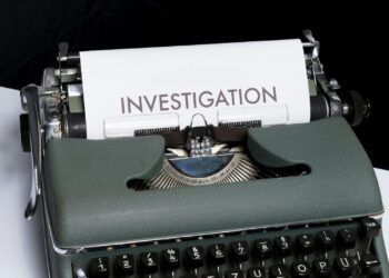 Yeşil renkli eski tip daktilonun üzerinde investigation yazılı kağıt var.