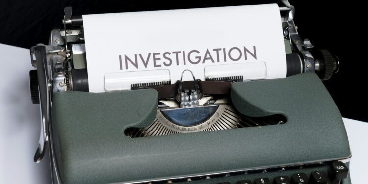 Yeşil renkli eski tip daktilonun üzerinde investigation yazılı kağıt var.