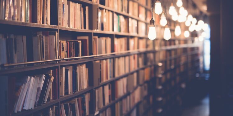 Kütüphanede sıra sıra dizilmiş kitap rafları ve asılı lambalar