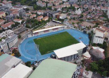 Havadan çekilmiş, mavi tartan pistli ve yeşil sahanlı bir spor kompleksi.