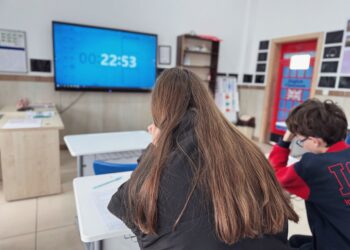 Sınıfta sırada oturan uzun saçlı bir kız öğrenci ve dijital ekran.