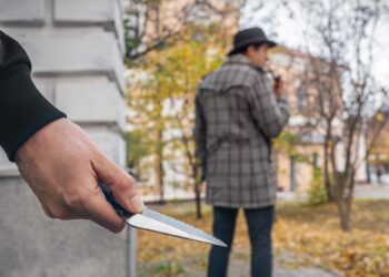 Sokakta elinde bıçak tutan bir şahıs ve arka planda yürüyen insan silüeti.