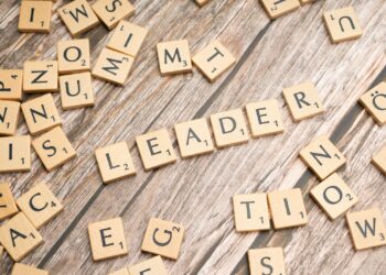 Ahşap masa üzerinde 'leader' kelimesini oluşturan Scrabble taşları ve etrafta rastgele harfler.