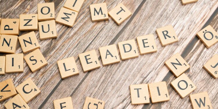 Ahşap masa üzerinde 'leader' kelimesini oluşturan Scrabble taşları ve etrafta rastgele harfler.