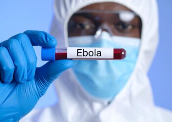 Koruyucu kıyafetli bir sağlık çalışanı üzerinde 'Ebola' yazan kan tüpü tutuyor.