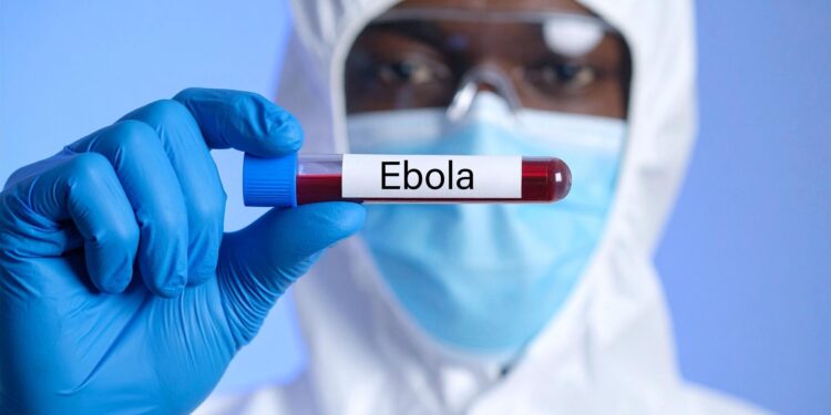 Koruyucu kıyafetli bir sağlık çalışanı üzerinde 'Ebola' yazan kan tüpü tutuyor.