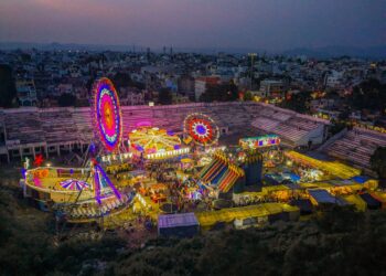 Aydınlatılmış dönme dolap ve lunapark oyuncaklarının gece havadan çekilmiş renkli görünümü.