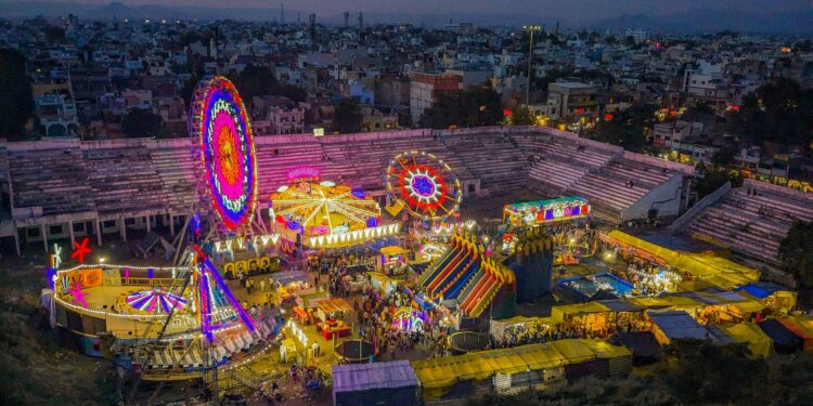 Aydınlatılmış dönme dolap ve lunapark oyuncaklarının gece havadan çekilmiş renkli görünümü.