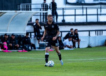 Futbol sahasında top süren ve siyah formasıyla dikkat çeken profesyonel erkek futbolcu.