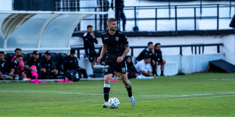 Futbol sahasında top süren ve siyah formasıyla dikkat çeken profesyonel erkek futbolcu.