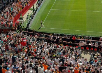 Yukarıdan çekilen stadyum tribünlerinde maç izleyen kalabalık futbol seyircileri ve çim saha.
