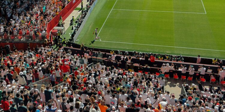 Yukarıdan çekilen stadyum tribünlerinde maç izleyen kalabalık futbol seyircileri ve çim saha.