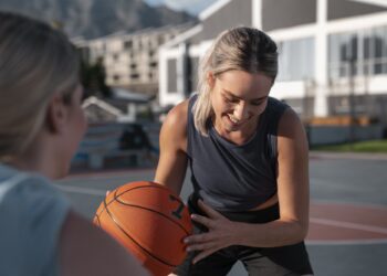 Saha kenarında elinde basketbol topu tutarak gülen kadın basketbolcu.
