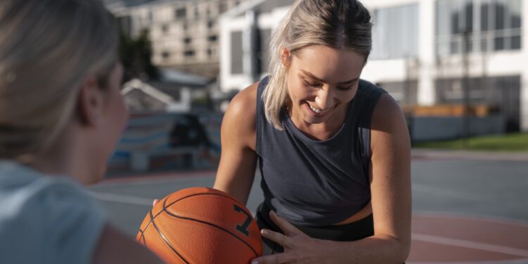 Saha kenarında elinde basketbol topu tutarak gülen kadın basketbolcu.