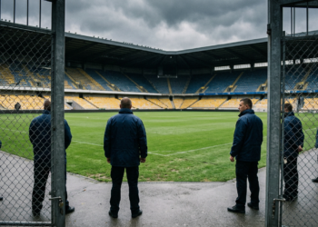 Futbol sahasına bakan, güvenlik görevlisi kıyafetli kişilerin arkadan görüldüğü stat kapısı.