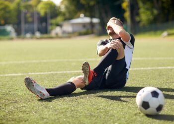 Saha çimlerinde oturmuş, bacağını tutarak acı çeken futbolcu