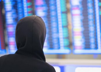 Kapüşonlu bir kişinin arkadan görünümü ve mavi dijital pano.