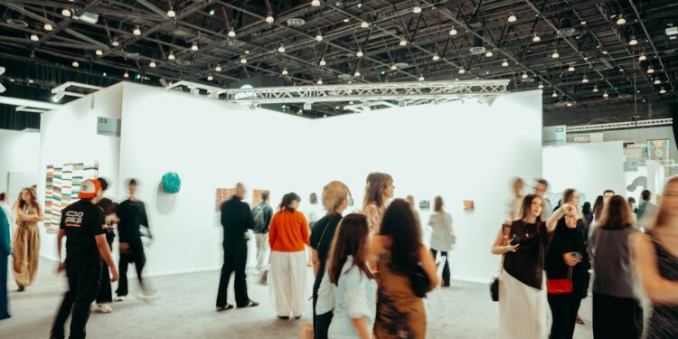 Geniş bir sanat galerisinde gezinen kalabalık sanatseverler ve sergilenen tablolar