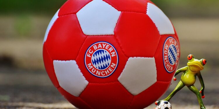 FC Bayern München logolu kırmızı beyaz futbol topu ve yeşil kurbağa figürü.