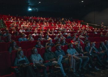 Karanlık bir sinema salonunda film izleyen kalabalık izleyici grubu.