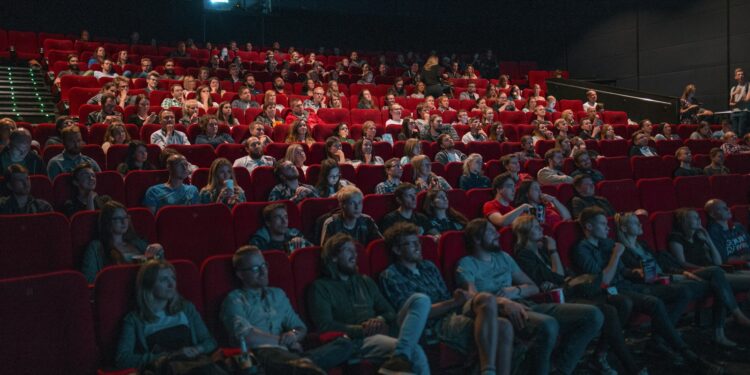 Karanlık bir sinema salonunda film izleyen kalabalık izleyici grubu.