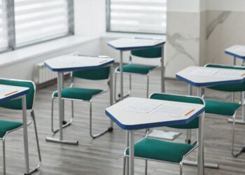 Sınıfta düzenli yerleştirilmiş tekli sınav masaları ve üzerinde soru kitapçıkları bulunuyor.