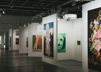 Geniş beyaz duvarlı bir çağdaş sanat fuarında sergilenen büyük tablolar.