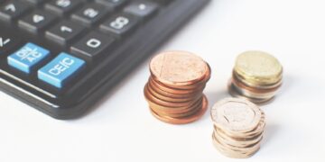 Siyah bir hesap makinesi ve üzerinde para biriktirilen madeni para yığınları.