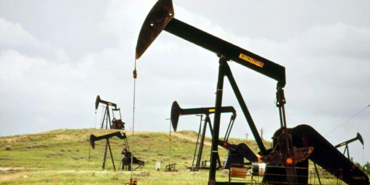 Arazide çalışan siyah renkli petrol kuyusu pompaları, bulutlu gökyüzü altında duruyor.