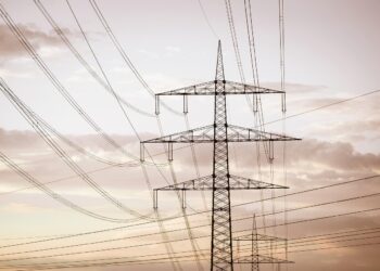 Gün batımı gökyüzü altında birbirine bağlı elektrik iletim hatları ve yüksek gerilim direkleri.