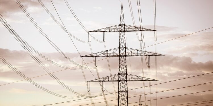 Gün batımı gökyüzü altında birbirine bağlı elektrik iletim hatları ve yüksek gerilim direkleri.