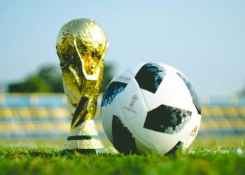 Çim saha üzerinde altın renkli dünya kupası kupası ve futbol topu.