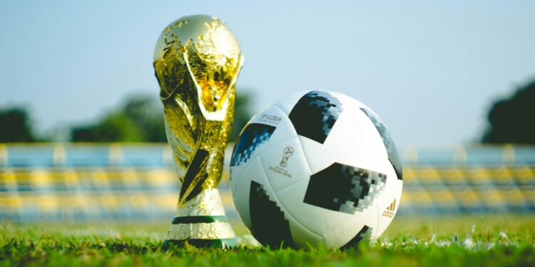 Çim saha üzerinde altın renkli dünya kupası kupası ve futbol topu.
