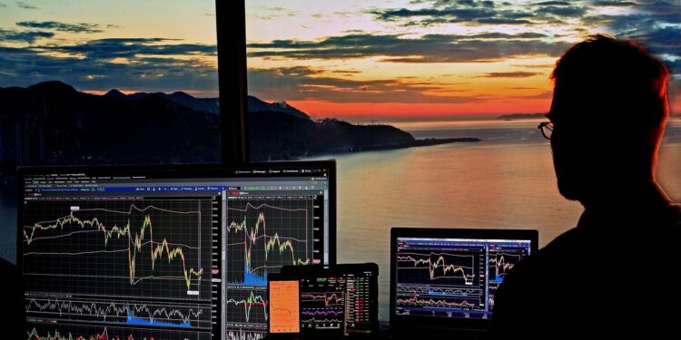 Gün batımı manzarasında borsa ve finans grafikleri inceleyen bir adam.