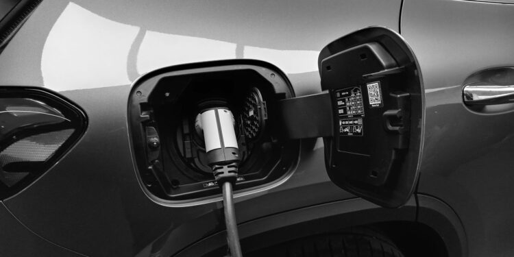 Gri renkli bir elektrikli otomobilin şarj kapağı açık ve şarj ediliyor.