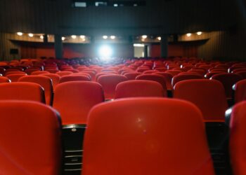 Kırmızı koltuklu sinema salonunda arkadan görünen koltuklar ve önde projektör ışığı