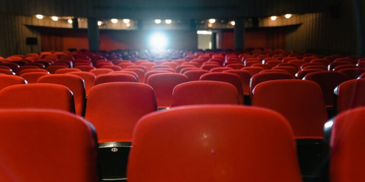 Kırmızı koltuklu sinema salonunda arkadan görünen koltuklar ve önde projektör ışığı