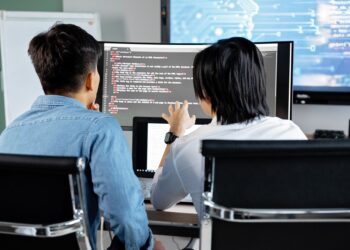 Ofiste bilgisayar ekranındaki kodları inceleyen iki genç erkek çalışan.