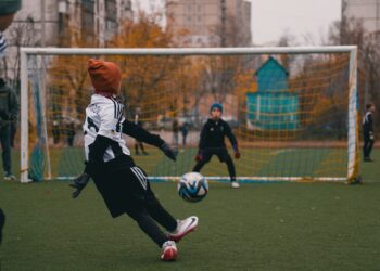 Futbol sahasında fileler önünde topa vuran sporcu ve kaleci