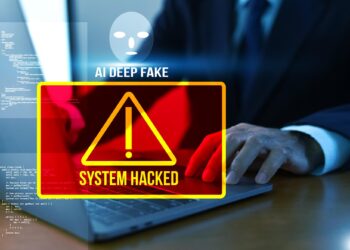 Bilgisayar başında çalışan bir kişinin önünde sistem hacklendi yazısı ve ikaz işareti bulunuyor.