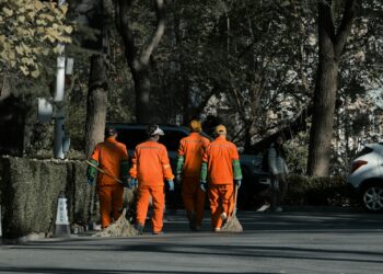 Sokakta turuncu kıyafetleriyle temizlik yapıp süpüren belediye işçileri.